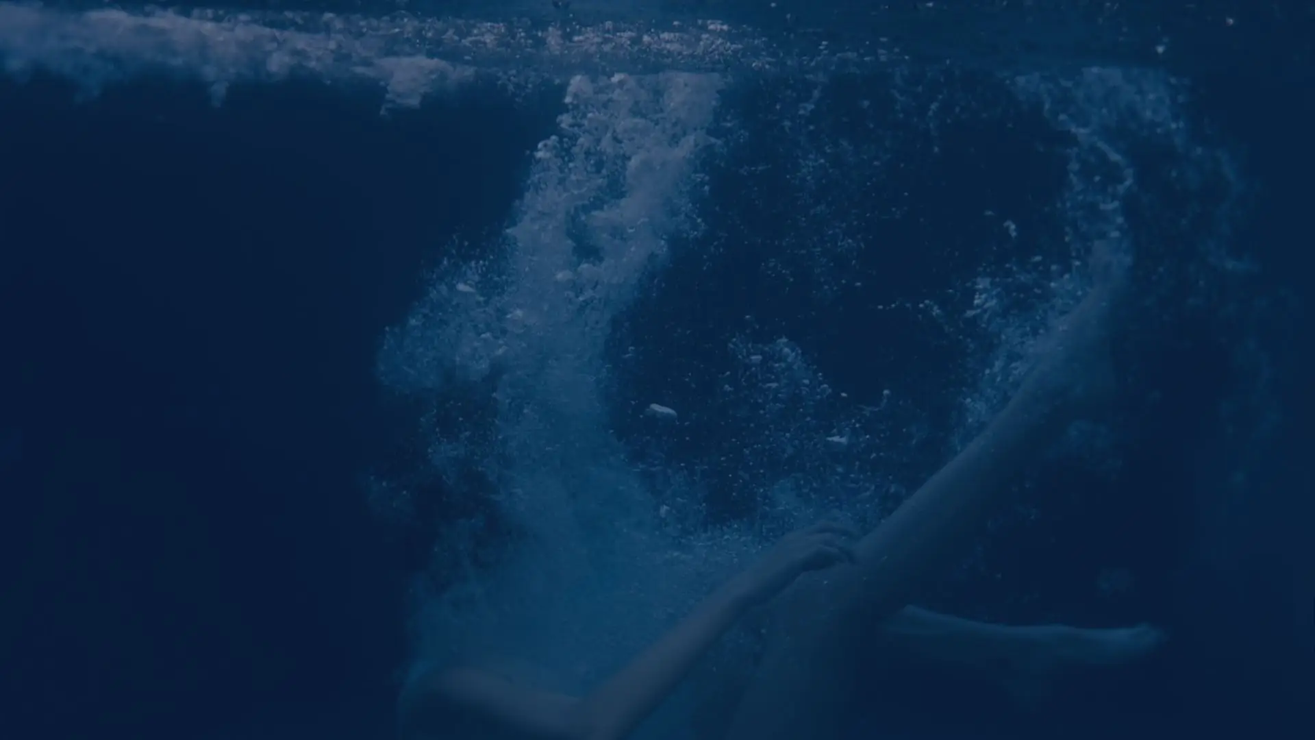 An underwater view of a person's arms in deep blue water, surrounded by rising bubbles.