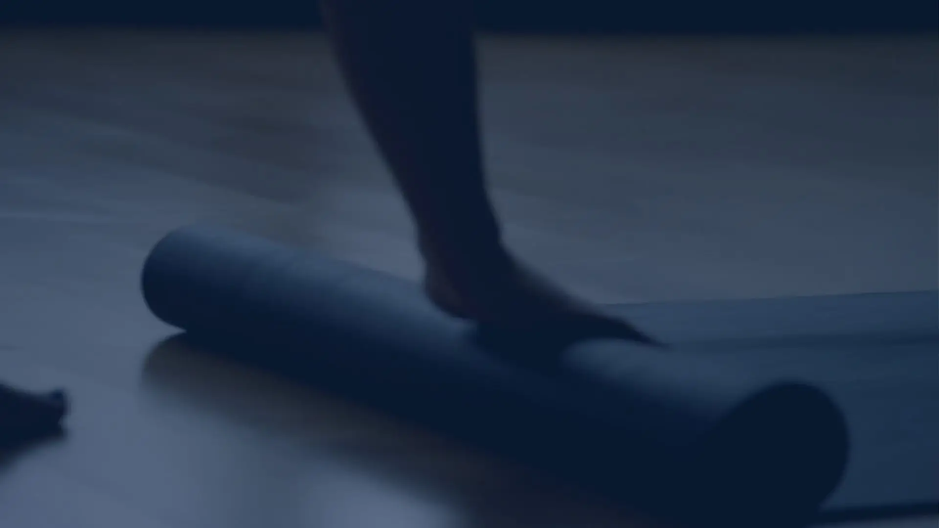 A yoga mat being unrolled across a studio floor, bare feet beside it.